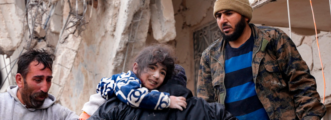 Indbyggere redder et lille barn ud af murbrokkerne efter jordskælvet i byen Jandaris, der ligger uden for Afrin i Syrien.